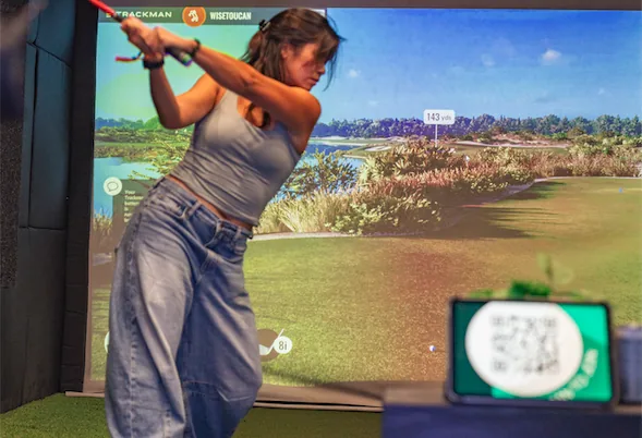 Golfer mid-swing inside a Dryvebox simulator with TrackMan shot data overlaid on screen